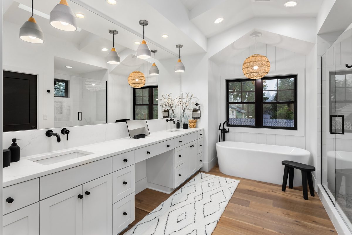 A white bathroom with a long double vanity, black tapware, a cluster of hanging pendant lights and a freestanding bath